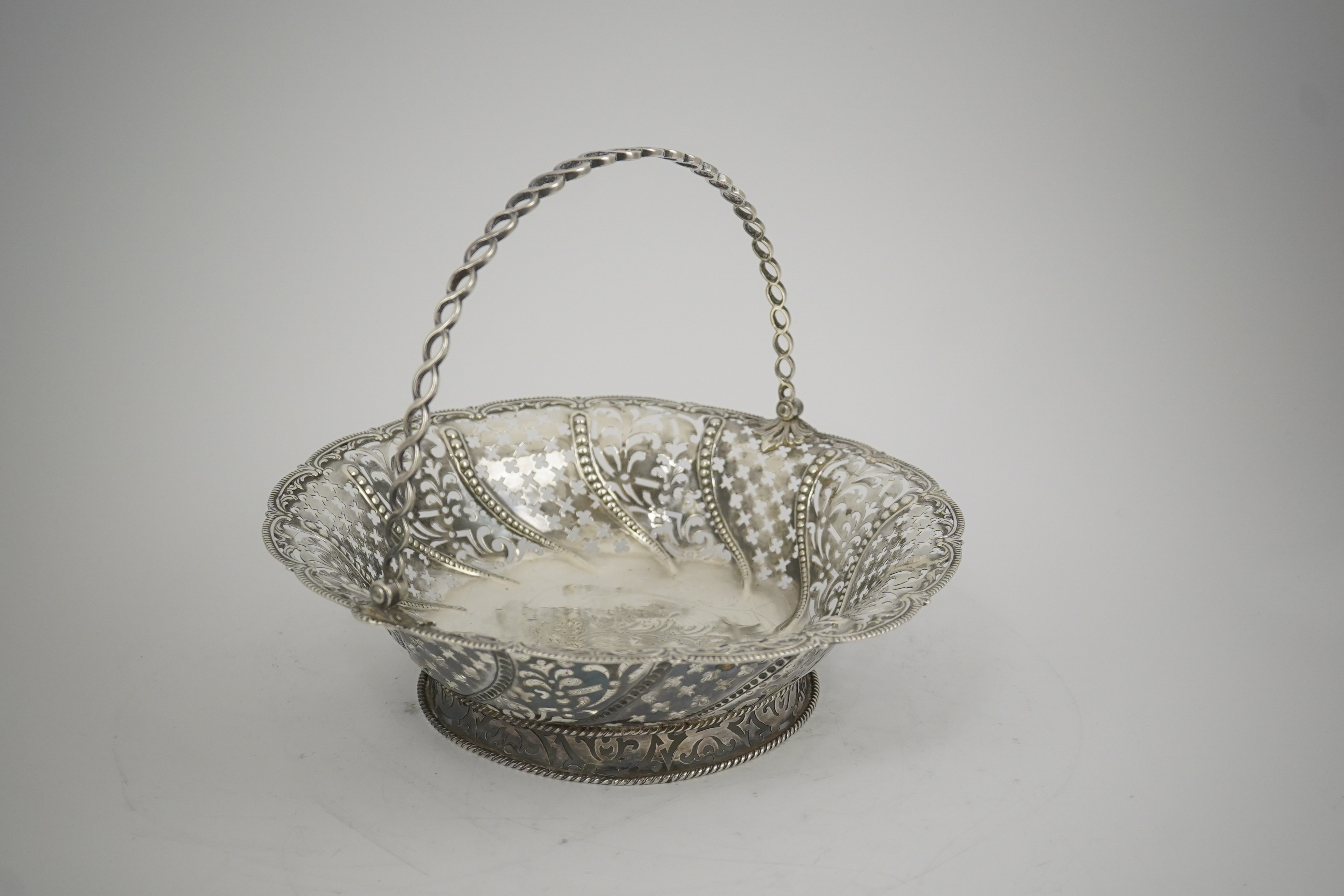 A late George II pierced silver cake basket, by William Plummer?, of shaped circular form, with engraved crest and multi ring handle, London, 1759, diameter 29.2cm, 25.5oz. (a.f.). Condition - poor